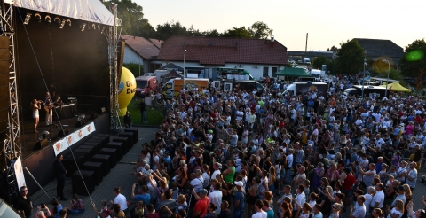Impreza "Dusznickie lato" w Dusznikach. Na zdjęciu uczestnicy koncertu. Po lewej stronie scena koncertowa w tle budynek przedszkola oraz strefa gastronomiczna - foodtrucki. Zdjęcie z konta facebook BPiCAK.