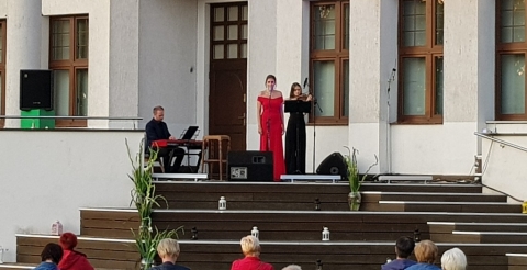 Na zdjęciu Joanna Aleksandrowicz z muzykami towarzyszącymi na tarasie CAK w Dusznikach. Na pierwszym planie słuchacze koncertu. 