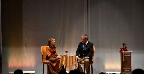 Na zdjęciu dwoje aktorów spektaklu "Tysiąc franków Norwida" na scenie. Aktorzy siedzą przy stoliku i rozmawiają.