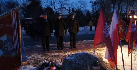 Uroczystość 103. rocznicy wybuchu Powstania Wielkopolskiego pod tablicą pamiątkową na skwerze przy ul. Powstańców Wielkopolskich. Na zdjęciu trzyosobowa delegacja Zarządu Gminnego OSP przed tablicą.