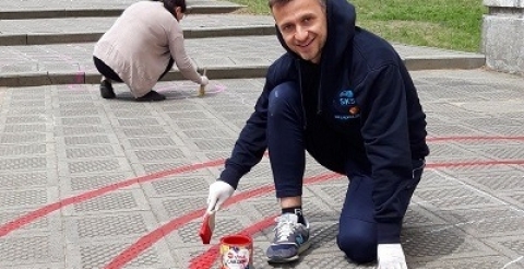 Na zdjęciu nauczyciele szkoły malujący kolorowe linie na chodniku przed szkołą.  