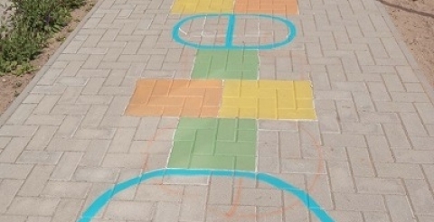 Na zdjęciu kolorowe koła i kwadraty namalowane na chodniku przed szkołą.