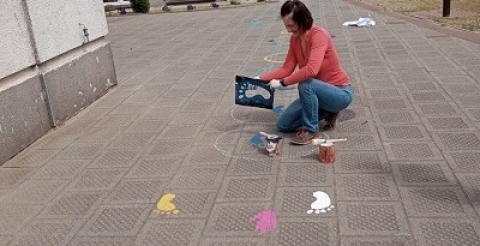 Na zdjęciu nauczycielka szkoły malująca kolorowe elementy trasy na chodniku przed szkołą.  