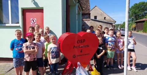 Na zdjęciu dzieci przy pojemniku na kapsle w kształcie serca. 