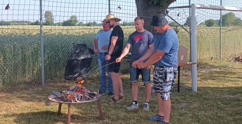 Festyn rodzinny w Kunowie. Na zdjęciu mężczyźni pieką kiełbaski nad ogniskiem.