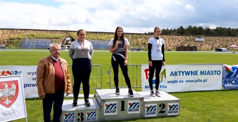 Na zdjęciu podium Mistrzostw Wielkopolski w Pile. Na najwyższym stopniu ze złotym medalem stoi Zuzanna Tyczyńska. W tle stadion sportowy.