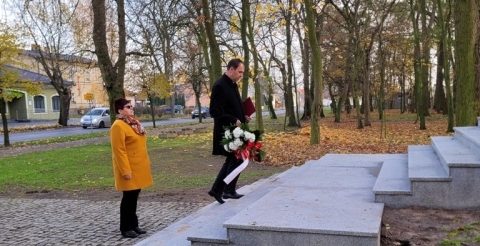 Delegacja z kwiatami zmierza w kierunku pomnika.