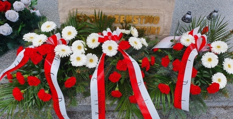 Na zdjęciu trzy wiązanki biało-czerwonych kwiatów z szarfami. 