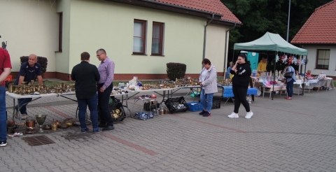 Stoiska z rękodziełem i starociami przy bibliotece w Dusznikach podczas Dożynek Gminnych 2021. Na pierwszym planie uczestnicy dożynek oglądający artykuły na stoiskach.